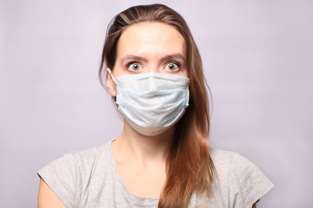 Une jeune femme porte un masque de protection respiratoire. Le chewing-gum est devenu gris de peur et ressemble à de grands yeux effrayés. Épidémie de grippe, allergie aux poussières. Coronavirus 2019 nCoV.