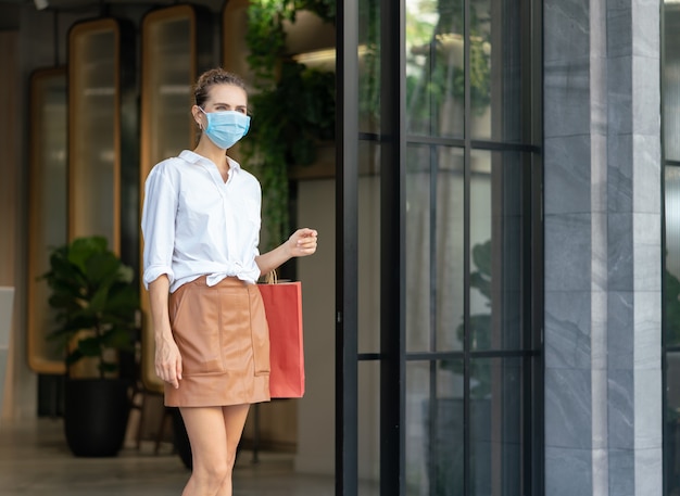 Jeune femme porter un masque médical de protection transportant des sacs de débrayage du centre commercial