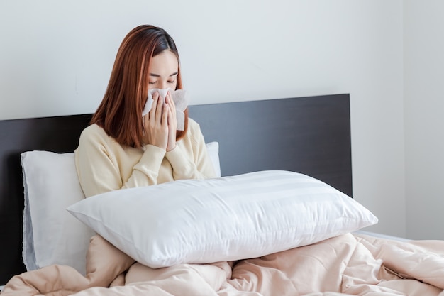 Jeune femme, porter, pull jaune, allergie nez, grippe, nez éternuer assis dans lit à la maison