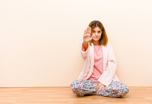 Jeune femme, porter, pyjama, séance, maison, regarder, sérieux, mécontent, colère, projection, paume ouverte, arrêt, geste