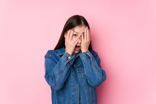 Jeune femme posant dans un mur rose isolé cligner des yeux effrayé et nerveux