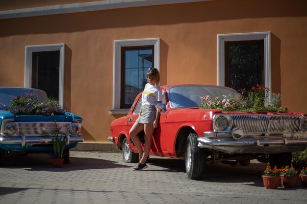 Une jeune femme pose devant une voiture abandonnée avec un jardin fleuri à la place du moteur