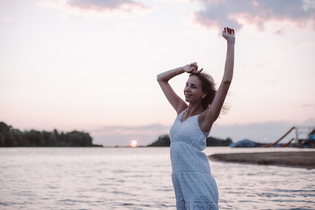 Une jeune femme pose sur fond de paysage une belle blonde heureuse dans un été blanc...