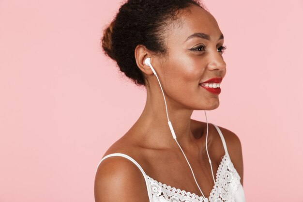 Jeune femme, poser, isolé, sur, mur rose, écoute, musique, à, écouteurs