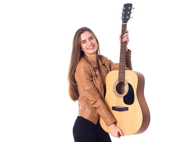 Jeune femme positive aux cheveux longs en veste marron et pantalon noir tenant une guitare et souriant sur fond blanc en studio