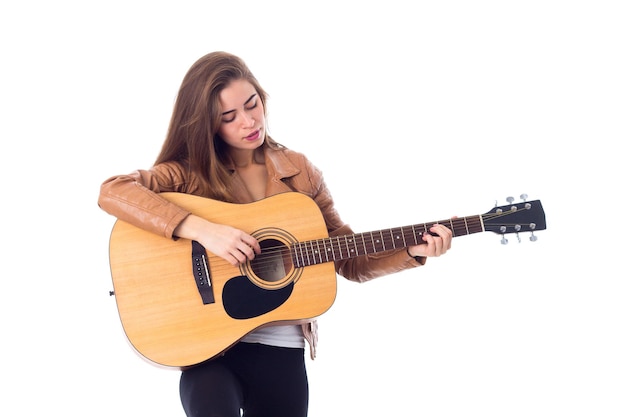 Jeune femme positive aux cheveux longs en veste marron et pantalon noir tenant une guitare en studio