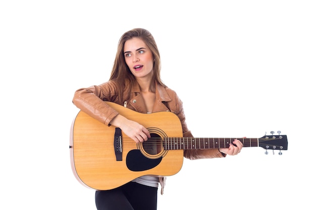 Jeune femme positive aux cheveux longs en veste marron et pantalon noir tenant une guitare en studio