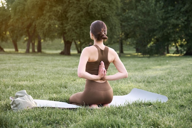 Une jeune femme positive dans un costume de gymnastique pratique le yoga et médite assise sur un tapis