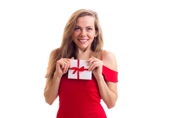 Jeune femme positive avec de longs cheveux bruns en robe rouge étriquée avec des boucles d'oreilles noires tenant présent