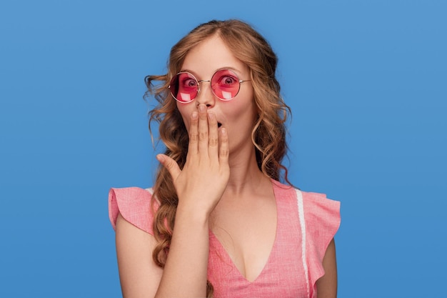 Jeune femme positive surprise en lunettes de soleil roses et robe élégante légère