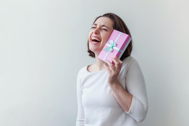 Jeune femme positive tenant une petite boîte cadeau rose isolée sur fond blanc préparation pour les vacances...