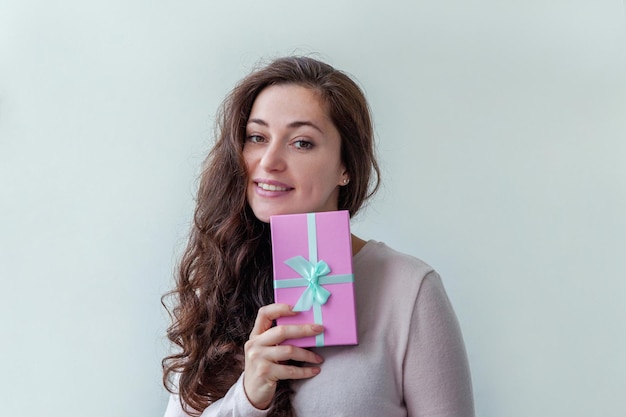 Jeune femme positive tenant une petite boîte cadeau rose isolée sur fond blanc préparation pour les vacances...
