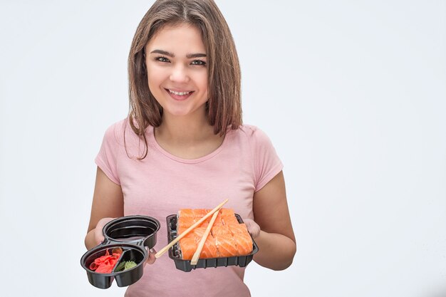 Une jeune femme positive tient la sauce soja avec du gingembre et des sushis dans les mains.