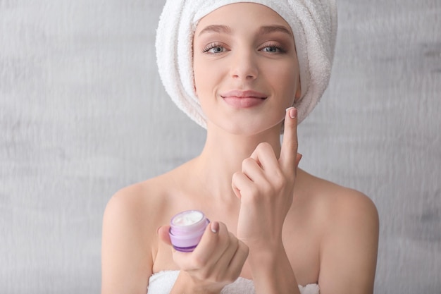 Jeune femme avec pot de crème sur fond gris