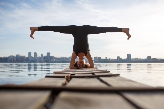 Jeune femme pratiquant des exercices d'yoga au quai en bois calme avec la ville. Sport et loisirs en pleine ville