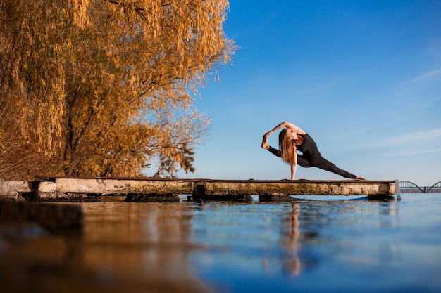 Jeune Femme Pratiquant Des Exercices D'yoga Au Quai En Bois Calme Avec Ville