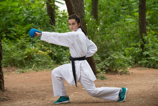 Jeune femme pratiquant ses mouvements de karaté dans la zone forestière boisée Kimono blanc ceinture noire
