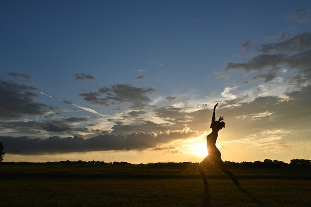 Jeune femme pratiquant le yoga à la campagne avec coucher de soleil