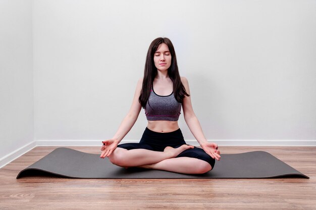 Jeune femme pratiquant le yoga à la maison médite sur un tapis en position du lotus