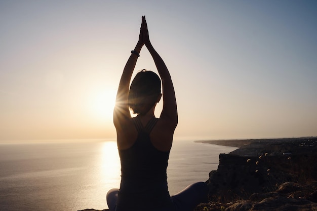 Jeune femme pratiquant le yoga sur la mer au coucher du soleil