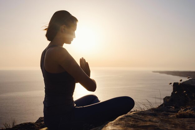 Jeune femme pratiquant le yoga sur la mer au coucher du soleil