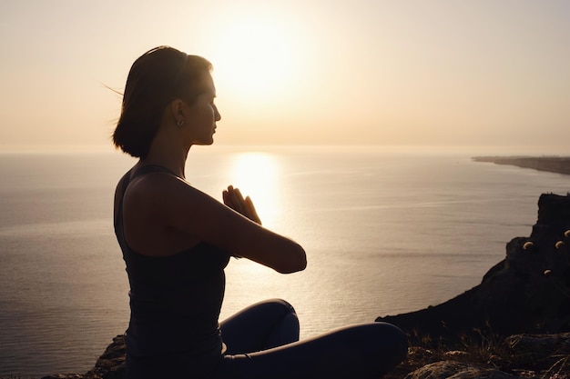 Jeune femme pratiquant le yoga sur la mer au coucher du soleil