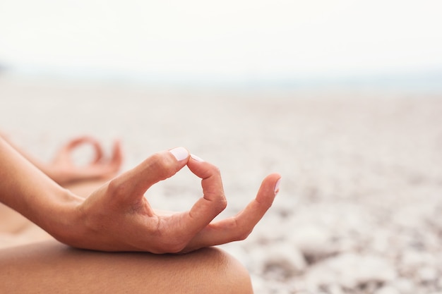 Jeune femme pratiquant le yoga sur la plage gros plan des mains gyan mudra et position du lotus