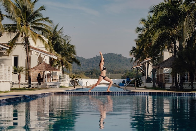 Jeune femme pratiquant le yoga pose sur la piscine et la plage de la nature au coucher du soleil ou au lever du soleil Yoga et Healthy Concept Warrior I ou Virabhadrasana Pose