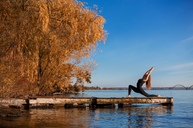 Jeune femme à pratiquer des exercices d'yoga au quai en bois calme avec fond de ville. Sport et loisirs en pleine ville