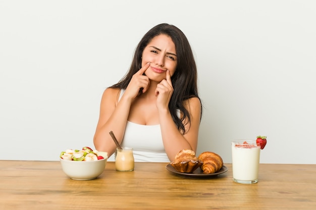 Jeune femme prenant un petit déjeuner en doutant entre deux options.