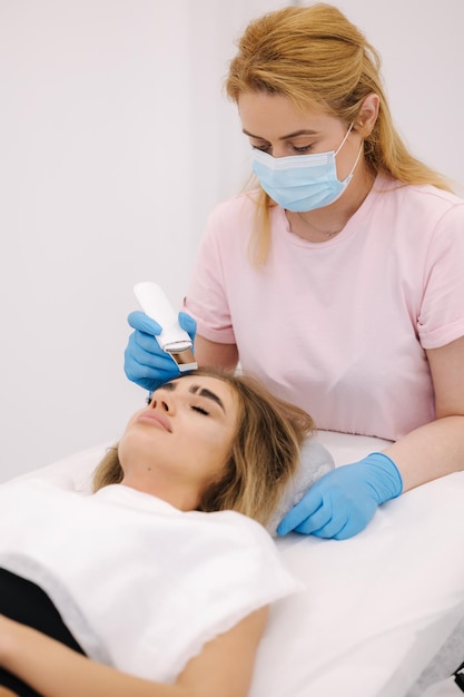 Jeune femme prenant une procédure de beauté dans un salon de spa esthéticienne à l'aide d'un dispositif d'épluchage à ultrasons