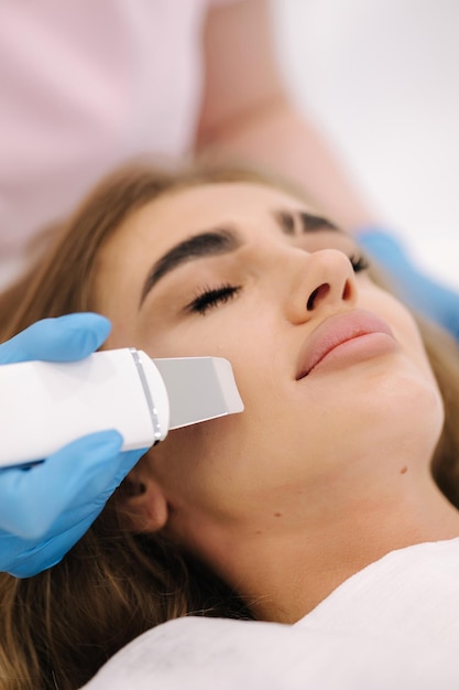 Jeune femme prenant une procédure de beauté dans un salon de spa esthéticienne à l'aide d'un dispositif d'épluchage à ultrasons