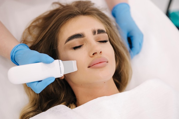 Jeune femme prenant une procédure de beauté dans un salon de spa esthéticienne à l'aide d'un dispositif d'épluchage à ultrasons