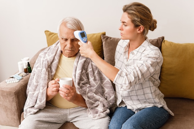 Jeune femme prenant soin de son grand-père âgé avec des symptômes de rhume à la maison