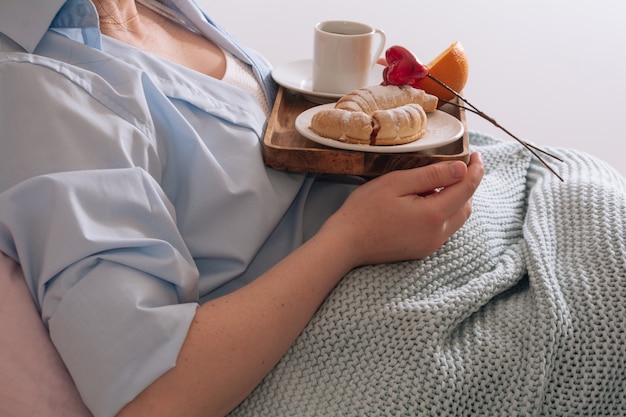 Jeune femme prenant son petit déjeuner dans un lit à la maison croissant orange et une tasse de café