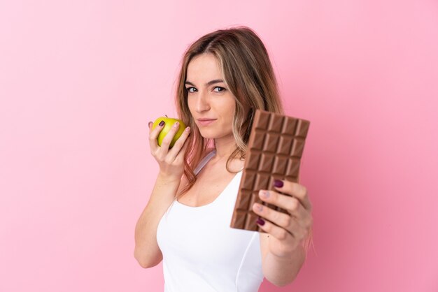 Jeune femme prenant une tablette de chocolat dans une main et une pomme dans l'autre