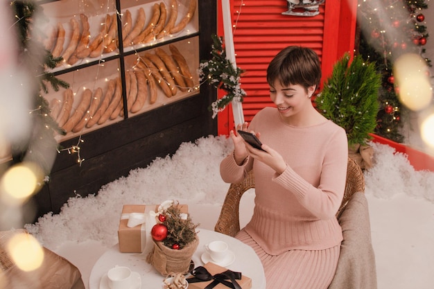 La jeune femme prend la boîte-cadeau de photo sur la table de fête avec la composition de sapin, temps de Noël