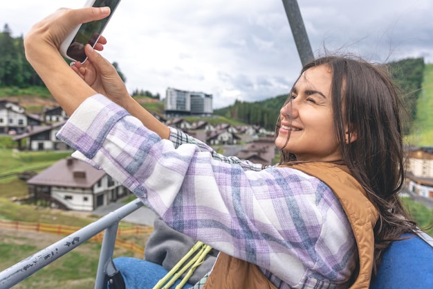 Une jeune femme prend un selfie sur un funiculaire dans les montagnes