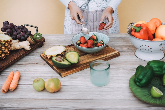 Jeune femme préparant une salade verte saine avec des légumes et des fruits - Concentrez-vous sur la main tenant la fraise