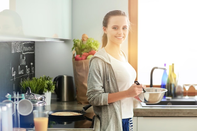 Jeune femme prépare des crêpes dans la cuisine tout en se tenant près de la table