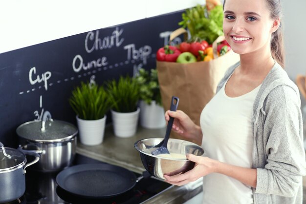 Jeune femme prépare des crêpes dans la cuisine tout en se tenant près de la table