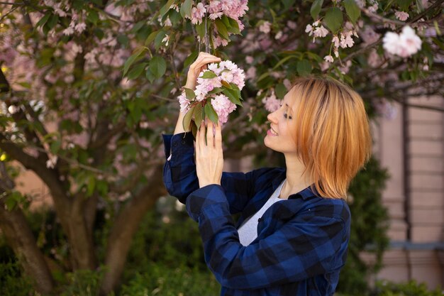 Jeune femme près de l'arbre en fleurs de sakura Fleurs roses concept de printemps et de jeunesse Fille élégante souriante