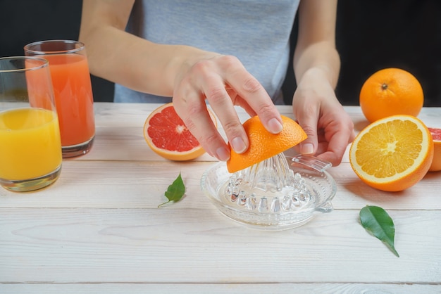 La jeune femme presse le jus d'orange à l'aide d'un presse-agrumes manuel en verre