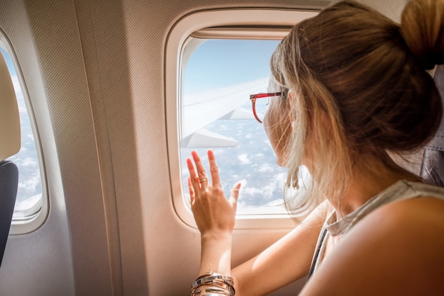 Jeune femme profitant de la vue à travers la fenêtre de l'avion assis pendant le vol dans l'avion