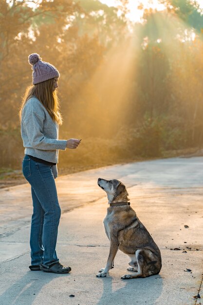 Jeune femme promenant son chien dans la nature avec les rayons du soleil du matin, lueur chaude et longues ombres