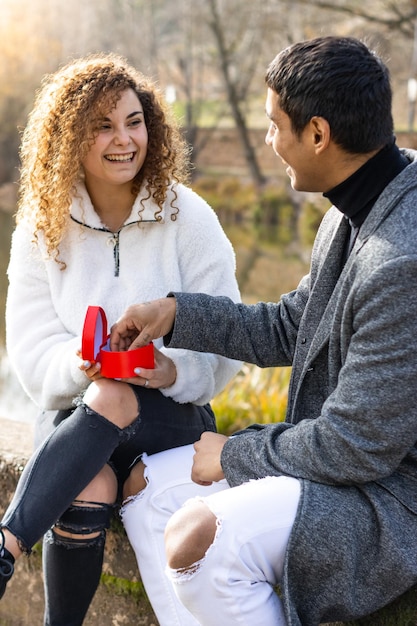 Jeune femme proposant à son petit ami à l'extérieur Fille assise faisant une demande en mariage à un petit ami latin souriant