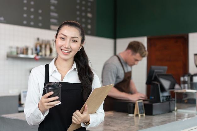 Jeune femme propriétaire de café barista souriant et tenant une tasse de café au café