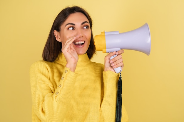 Jeune femme en pull chaud jaune avec haut-parleur mégaphone disant un secret