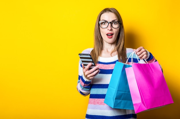 Jeune femme en pull détient des sacs à provisions et mobile