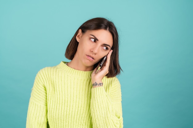 Jeune femme en pull vert clair avec téléphone portable ayant une conversation en écoutant un message audio